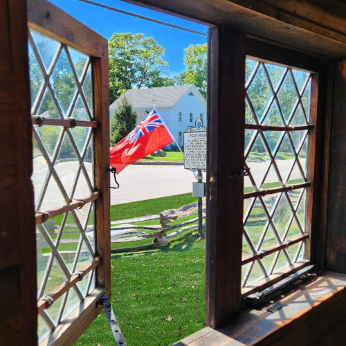 Peak House window taken from the inside, looking out towards front yard with flag